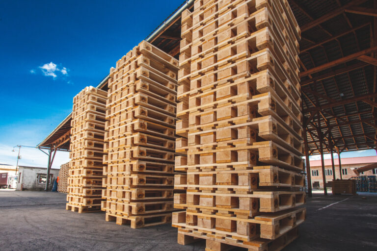 Wooden pallets stacked in rows. The pallets are located in the middle of the warehouse
